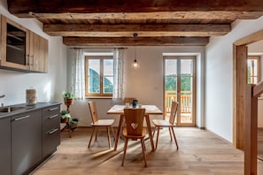 Cozinha com armários de madeira, uma mesa de jantar com cadeiras e vista para o exterior por grandes janelas.