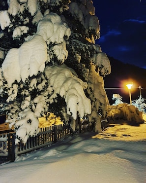 Eine verschneite Landschaft in der Nacht mit einem Zaun und einer Straßenlaterne.