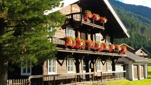 Ein traditionelles Holzchalet mit mehreren Balkonen, die mit Blumen geschmückt sind, umgeben von Wald und Bergen.