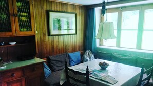 Ein gemütlicher Essbereich mit einer Holzwand, einem gerahmten Bild, einem Tisch mit Obstschale und einem Fenster mit Vorhängen.