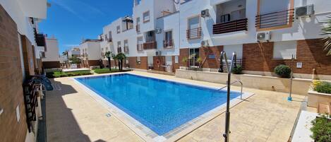 A swimming pool surrounded by modern buildings with balconies and air conditioning units.