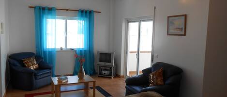 A living room with two sofas, a coffee table, a TV, and a sliding glass door leading to a balcony.