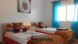 Une chambre avec deux lits, une table de chevet, une œuvre d’art murale et une fenêtre avec des rideaux.