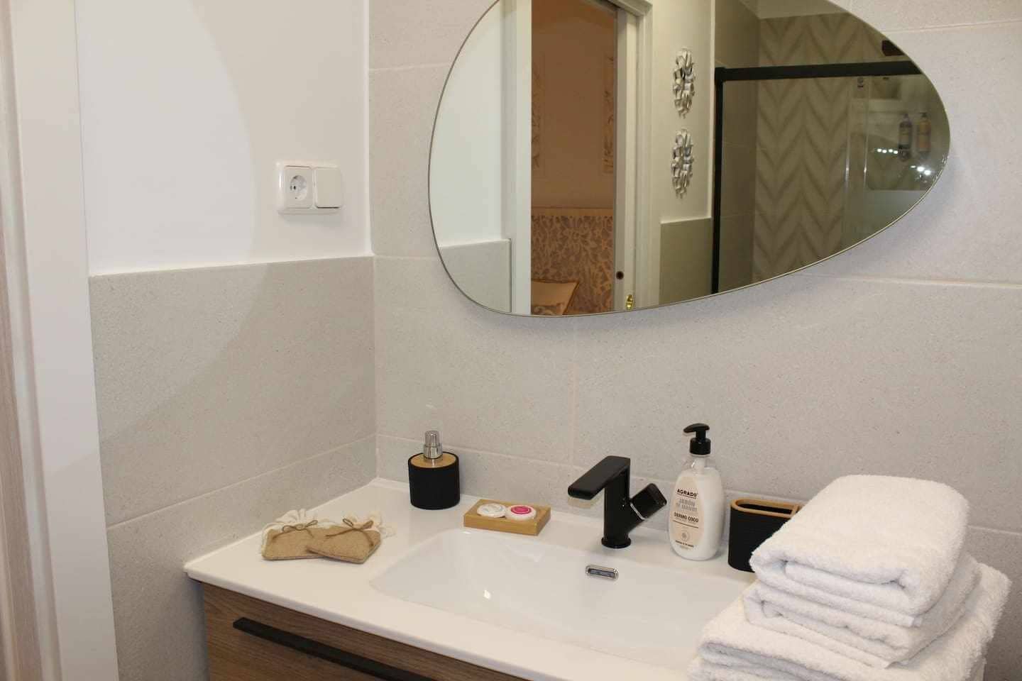 Ein Badezimmer mit einem weißen Waschbecken, einem Spiegel, einer schwarzen Armatur, einem Seifenspender, einem Handtuch und einem Toilettenpapierhalter.
