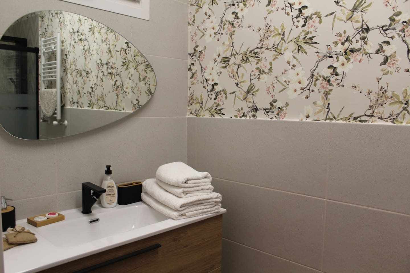 Un bagno con uno specchio, un lavandino, un portasciuga asciugamani e carta da parati floreale.