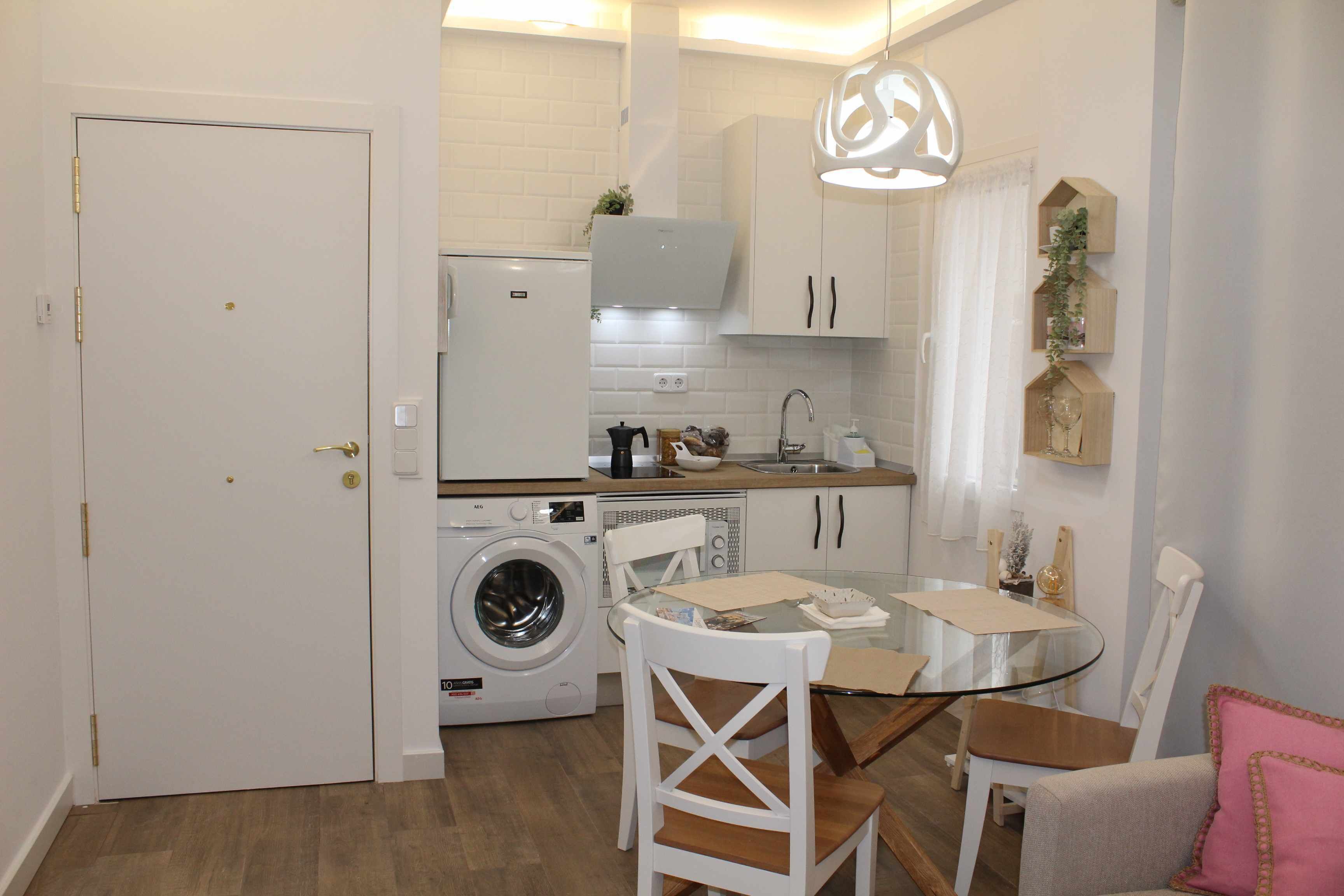 Une cuisine compacte équipée d’un lave-linge, d’une table à manger avec des chaises et d’un luminaire suspendu.