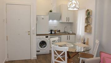 Une cuisine compacte équipée d’un lave-linge, d’une table à manger avec des chaises et d’un luminaire suspendu.