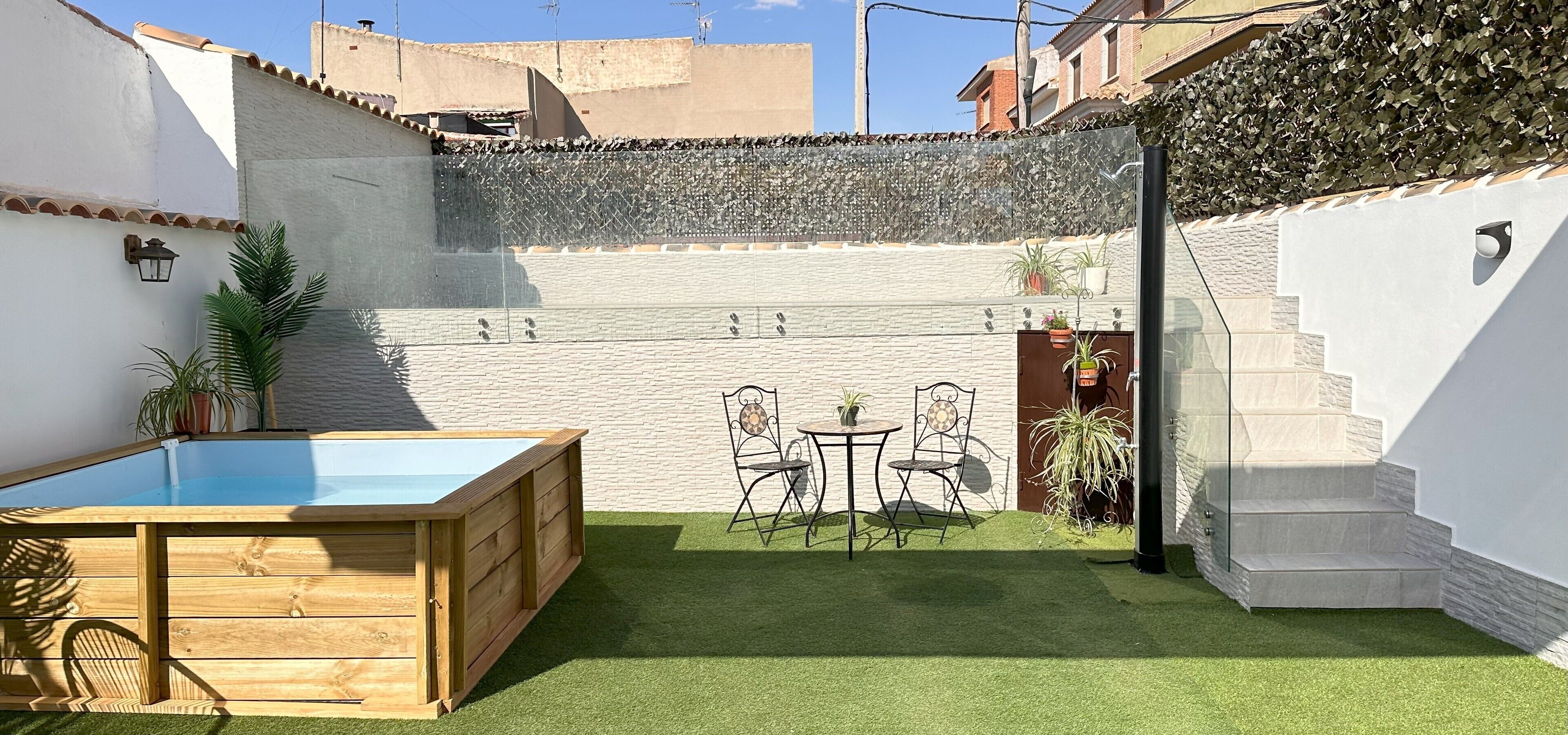 A small, enclosed patio with a wooden pool table, a small table with chairs, and a staircase leading to an upper level.