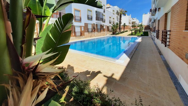 Una piscina amb terrassa enrajolada, envoltada d'edificis blancs amb balcons i detalls de maó.