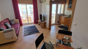 Un espai habitable compacte amb un sofà, una televisió, una taula de dinar amb cadires i una zona de cuina.