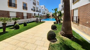 Un pati amb piscina, palmeres i un camí de rajola.