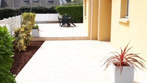 A courtyard with a gravel path, a white fence, a yellow building, and a table with chairs. - Detached house, facing south, av garage and enclosed garden, 350 m from the beach (Finistere (Clohars-Carnoët)