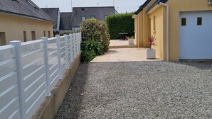 A courtyard with a gravel path, a white fence, and a hedge. - Detached house, facing south, av garage and enclosed garden, 350 m from the beach (Finistere (Clohars-Carnoët)