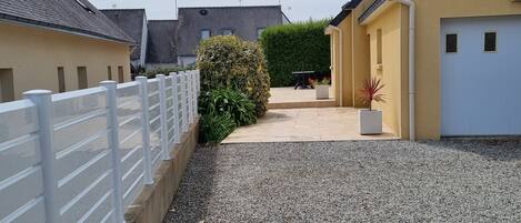 A courtyard with a gravel path, a white fence, and a hedge.