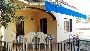 Un área de comedor al aire libre con techo, una pared de piedra, un toldo azul y una barandilla de metal negro.