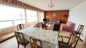 A dining area with a table set for four, a sofa, a television, and a chandelier. - 2-Bedroom Apartment with Balcony in Sables-d'Olonne (Les Sables-d'Olonne)