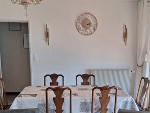 A dining area with a table set for four, wooden chairs, a wall clock, and a radiator.