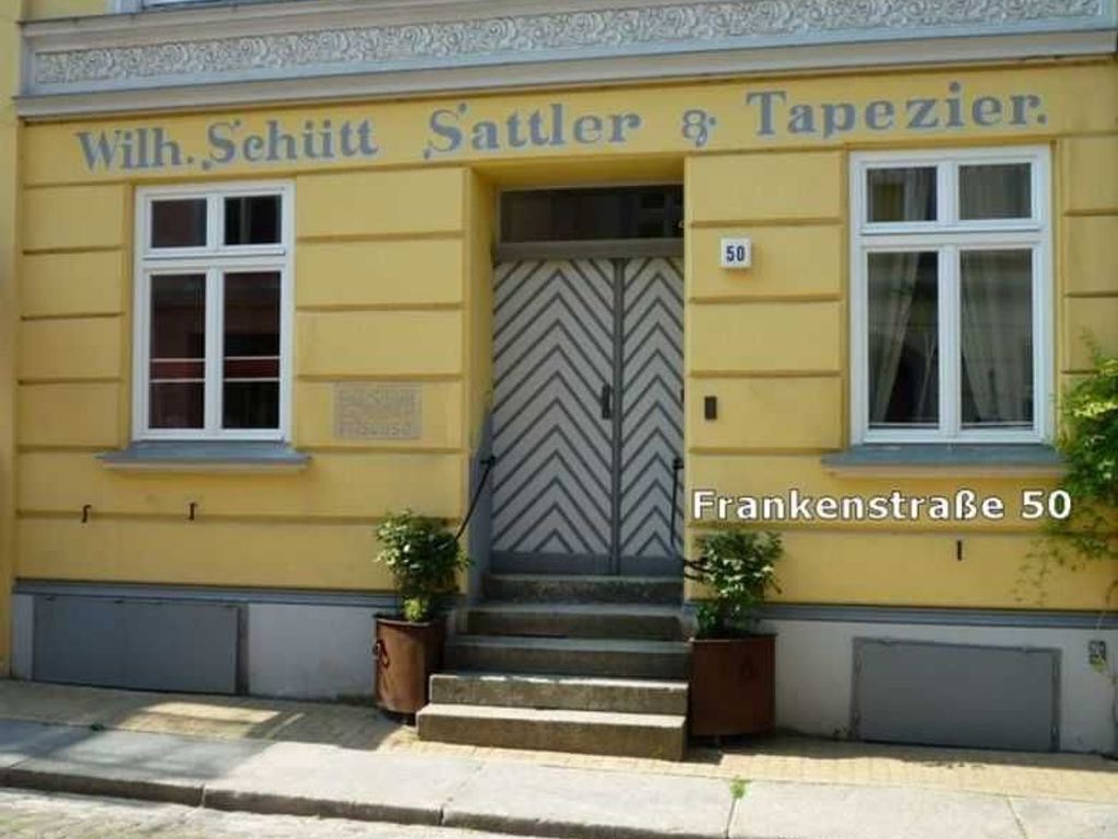 Un edificio amarillo con una puerta de diseño en forma de chevrón y el nombre "Wilh. Schütt Sattler & Tapezierer" sobre él.