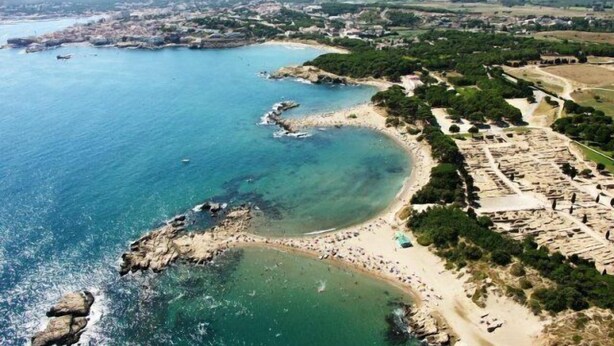 An aerial view of a coastal town with a beach, rocky shoreline, and residential areas.