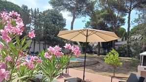 An outdoor patio area with a pool, outdoor furniture, and a pergola with an umbrella.