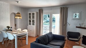 A cozy living room with a sofa, a dining table set for four, a cabinet, and a view of the outdoors.