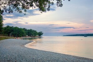 A pebbled beach with a calm sea, trees, and a distant shoreline. - Family-friendly large   apartment with 2 bathrooms for 6 - 8 pers (Porec)
