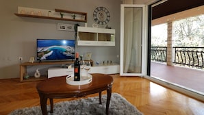 Una sala de estar con televisor, una mesa de madera, un reloj y un balcón con barandilla.