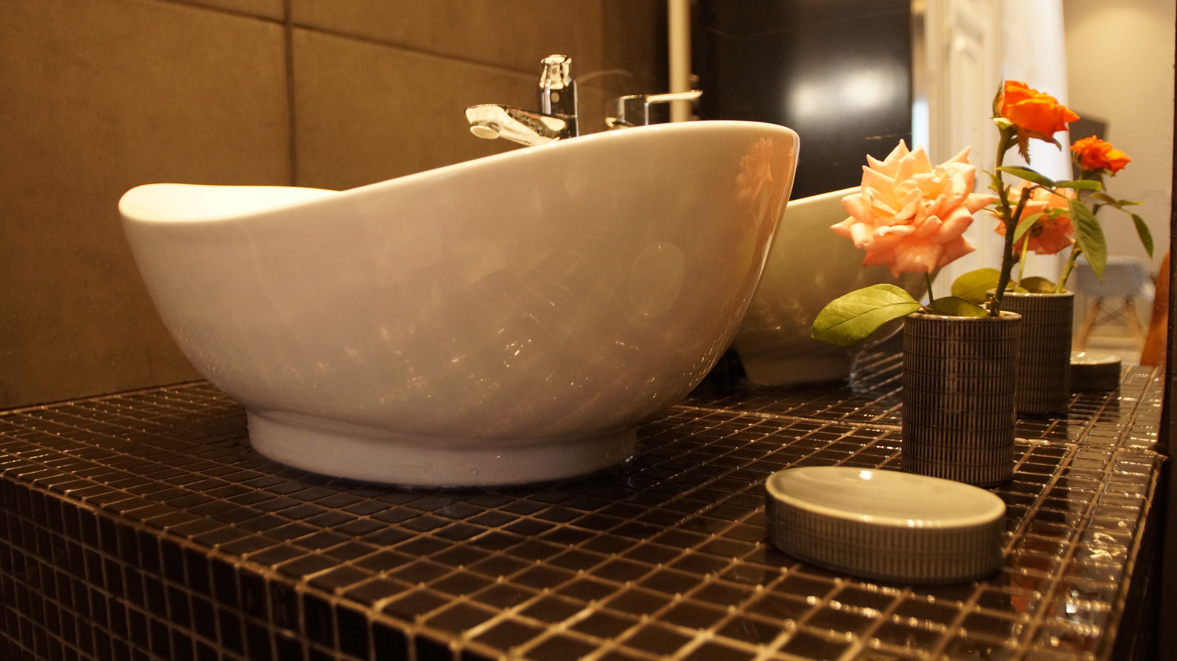 Een witte keramische wasbak met een modern design, geplaatst op een zwarte betegelde aanrecht.