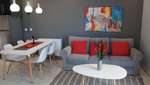 A modern living room with a grey sofa, red cushions, a white coffee table, and a dining area with a white table and chairs. - Luxury Apartment, Tranquility, Sea Views, Breeze (Agios Gordios, Kerkira)