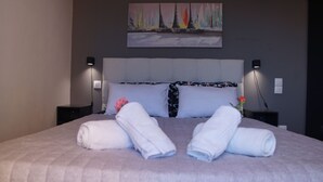A neatly made bed with towels and a rose, a painting on the wall, and two bedside lamps. - Luxury Apartment, Tranquility, Sea Views, Breeze (Agios Gordios, Kerkira)