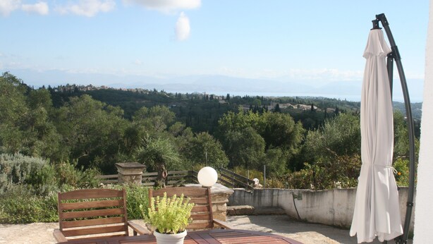 A wooden table with a potted plant, a wooden bench, and a white umbrella on a rooftop terrace with a view of a forested landscape. - Luxury Apartment, Tranquility, Sea Views, Breeze (Agios Gordios, Kerkira)