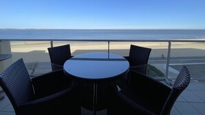 A balcony with a round table and four chairs, overlooking a beach and the ocean.
