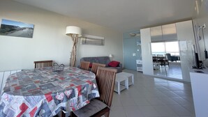 A spacious living area with a dining table, sofa, and a view of the sea through large windows.