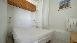 A small, single-bed room with a wooden cabinet above the bed, a wall-mounted radiator, and a framed picture on the wall.