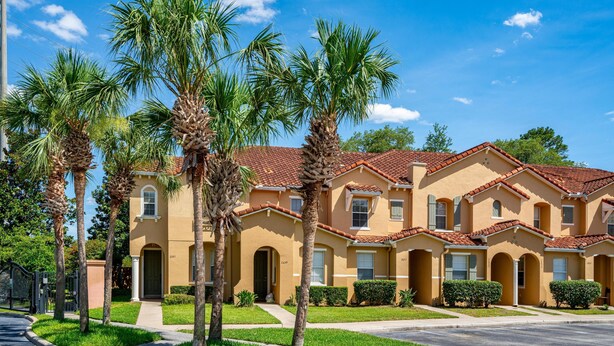 A row of two-story houses with a red-tiled roof, surrounded by palm trees and a well-maintained lawn.
