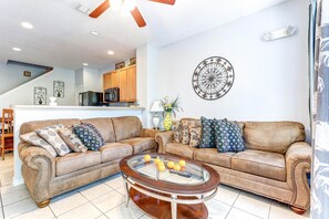 A living room with a brown leather sectional sofa, a glass coffee table with oranges, and a dartboard on the wall.