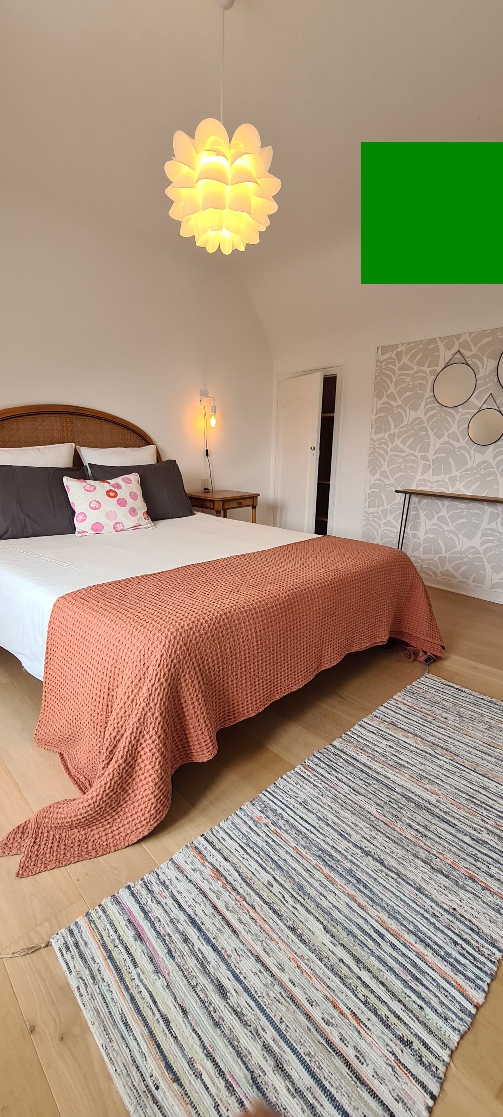 A bedroom with a bed, a hanging light fixture, a nightstand, and a patterned rug.