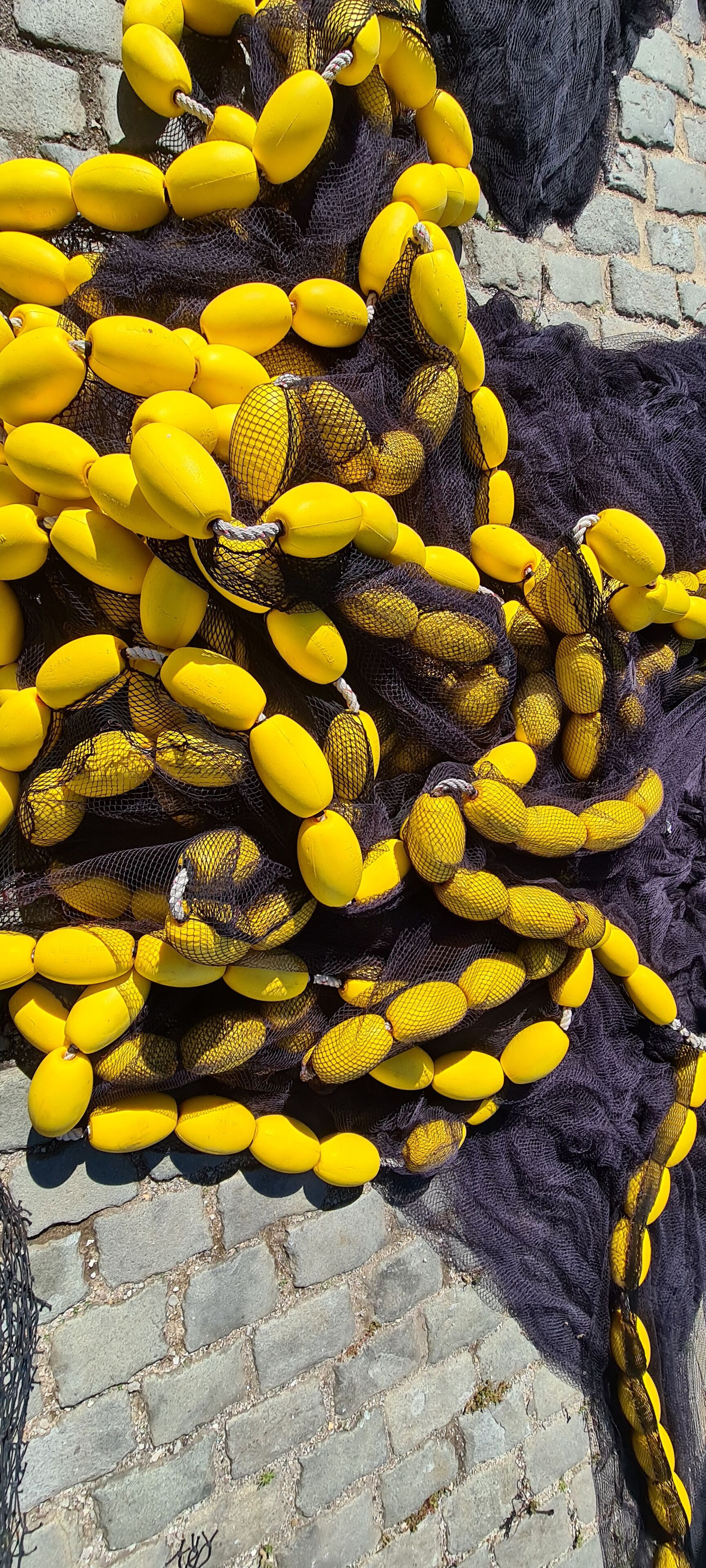 Um conjunto de objetos amarelos, possivelmente bananas, dispostos numa rede, apoiados em uma parede de pedra.