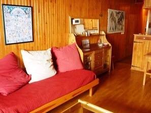 A wooden-floored room with a red sofa, a wooden cabinet, and a wall-mounted mirror.