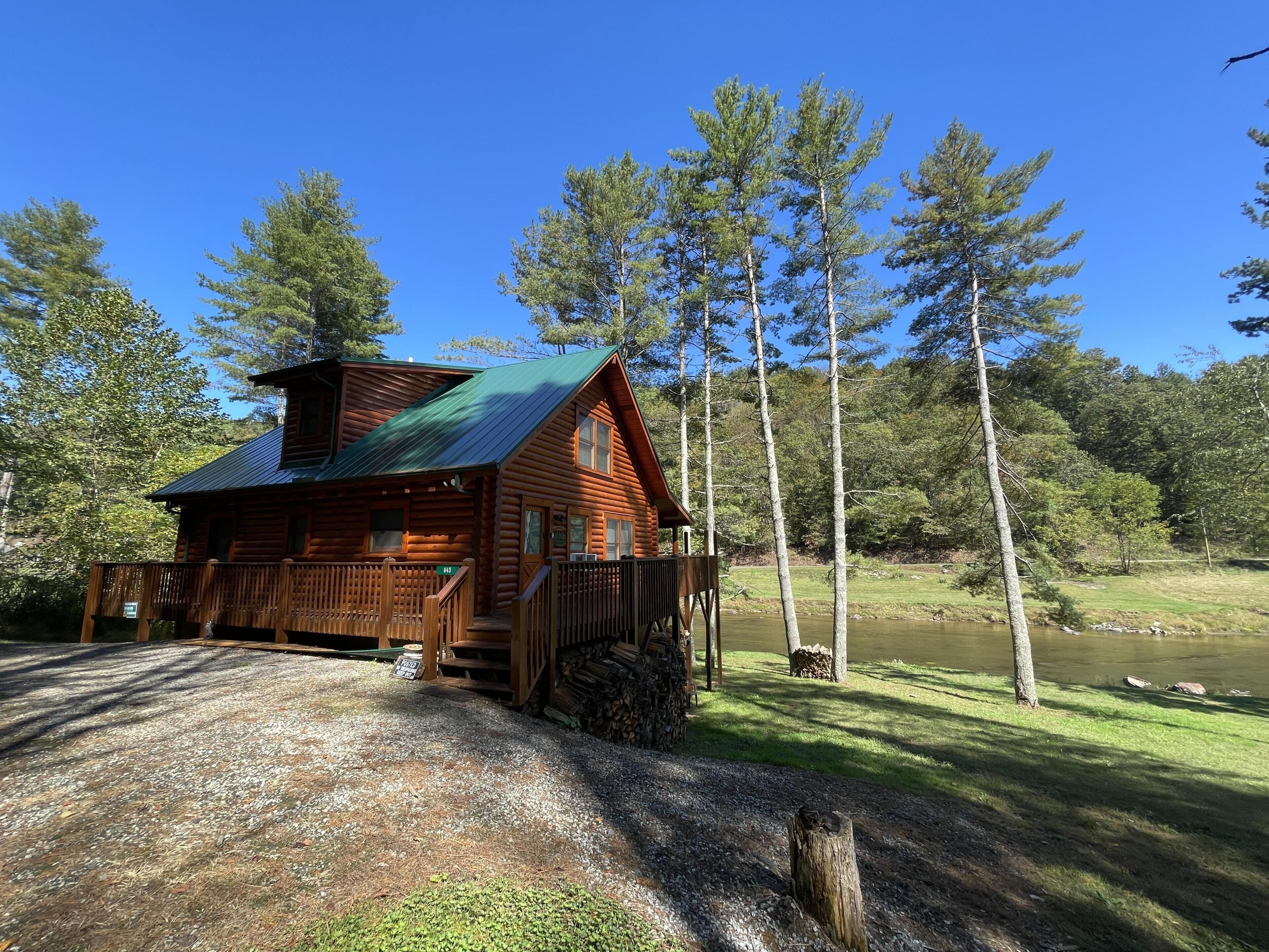 Une cabane en rondins avec une véranda, une terrasse couverte et une vue sur un lac.