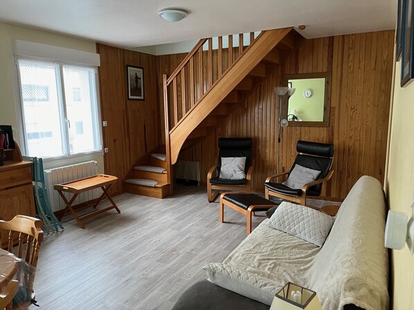 En hyggelig stue med en trætrap, en sofa, to lænestole og et lille bord.