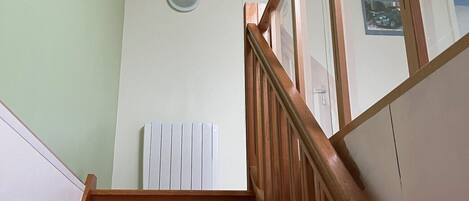 Een houten trap met een leuning, een radiator en een wandlamp.