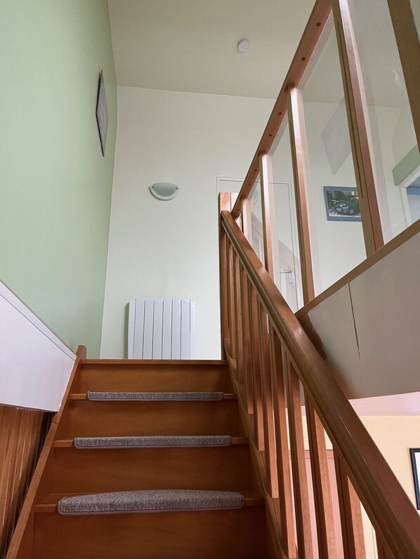 A wooden staircase with a handrail, a radiator, and a wall-mounted light fixture.