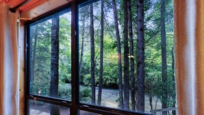Ein Zimmer mit großem Fenster und Blick auf ein bewaldetes Gebiet mit hohen Bäumen und einem Bach.