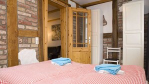 A room with a checkered bedspread, a wooden door, and a brick wall. - Apartment Westwind with view of churches - Gohr- apartments (Stralsund)