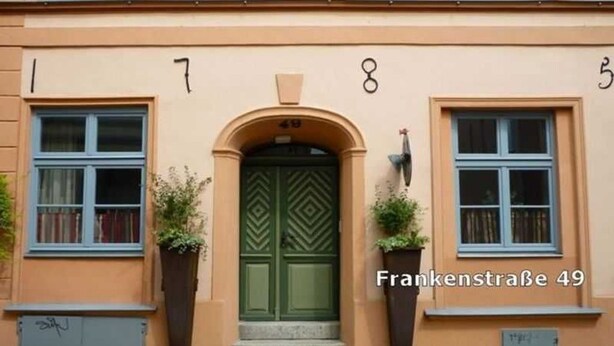 A building with the address Frankenstraße 49. It features a green door with a diamond pattern, flanked by two large planters with greenery. - Apartment Westwind with view of churches - Gohr- apartments (Stralsund)