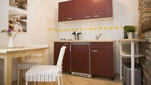 A compact kitchen with a dishwasher, a small refrigerator, and a dining area with a table and chairs. - Apartment Westwind with view of churches - Gohr- apartments (Stralsund)
