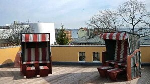 Two outdoor seating areas with striped cushions on a rooftop terrace, overlooking a cityscape. - Apartment Westwind with view of churches - Gohr- apartments (Stralsund)