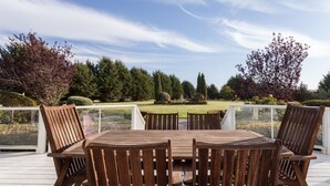 An outdoor wooden deck with a table and chairs, surrounded by a glass railing, overlooking a landscaped garden. - Perfect For Large Family Get Aways Or Your Gorgeous Ranch Style Wedding. (Arroyo Grande)