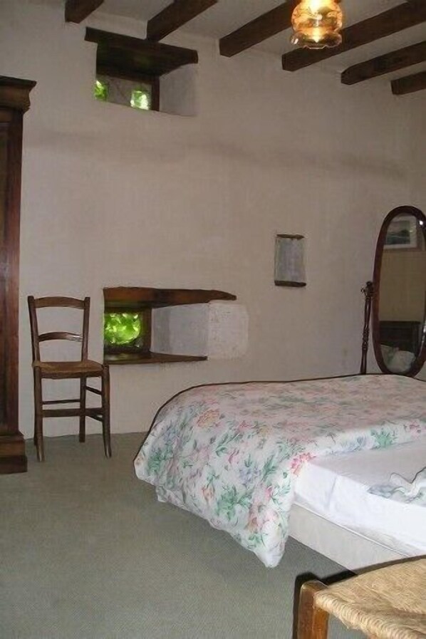 Une chambre à coucher avec un lit, une chaise, un bureau, un miroir et une petite fenêtre.